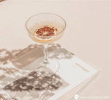 Champagne saucer with lemon inside on white background on top of a magazine