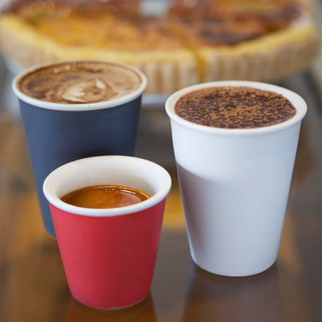 blue, red and white bevande coffee cups on a table with a dessert shown in the background