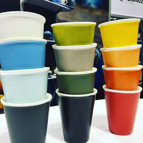 The columns of four different coloured latte cups with a cafe scene in background