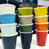 The columns of four different coloured latte cups with a cafe scene in background