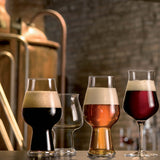 Four different shaped tulip style beer glasses, 3 with liquid and one clear on a table with a brewery background
