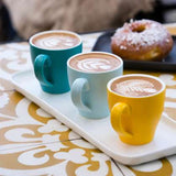 Three different coloured coffee mugs on white serving tray