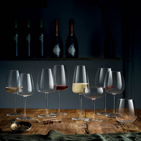A selection of nine different wine glasses with liquid on a wooden table top