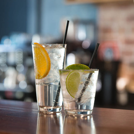 One large and one small, tapered tumblers both with liquid, garnish and straws presented on a blurred bar setting
