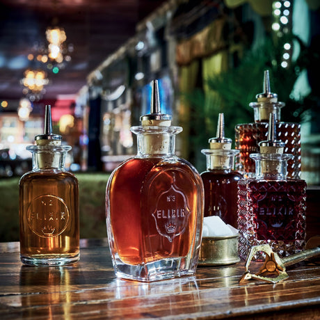 Five different bitters bottles all containing liquid on a bar setting background